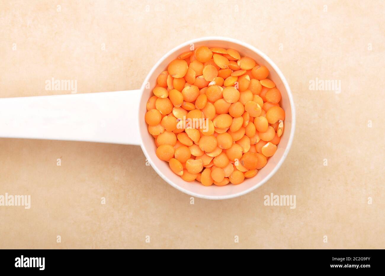 Red lentils on measuring spoon and brown background Stock Photo