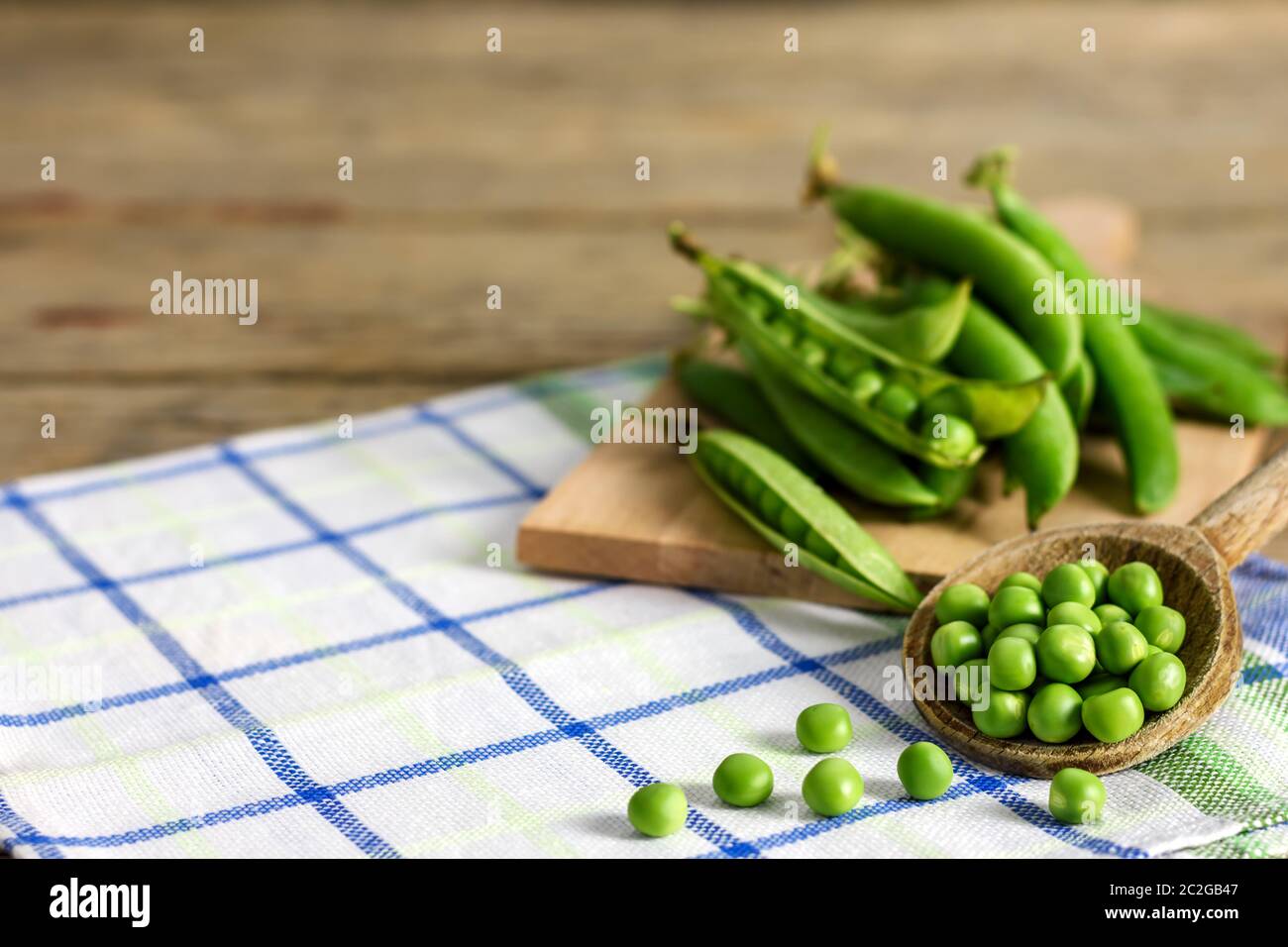 Fresh green peas on a wooden ladle and peas in pods on a kitchen cloth with copy space for text. Stock Photo