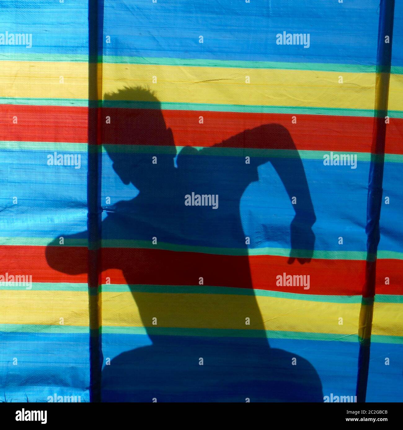 Shadow of dancing boy behind brightly coloured wind breaker on a hot summers day at the beach Stock Photo