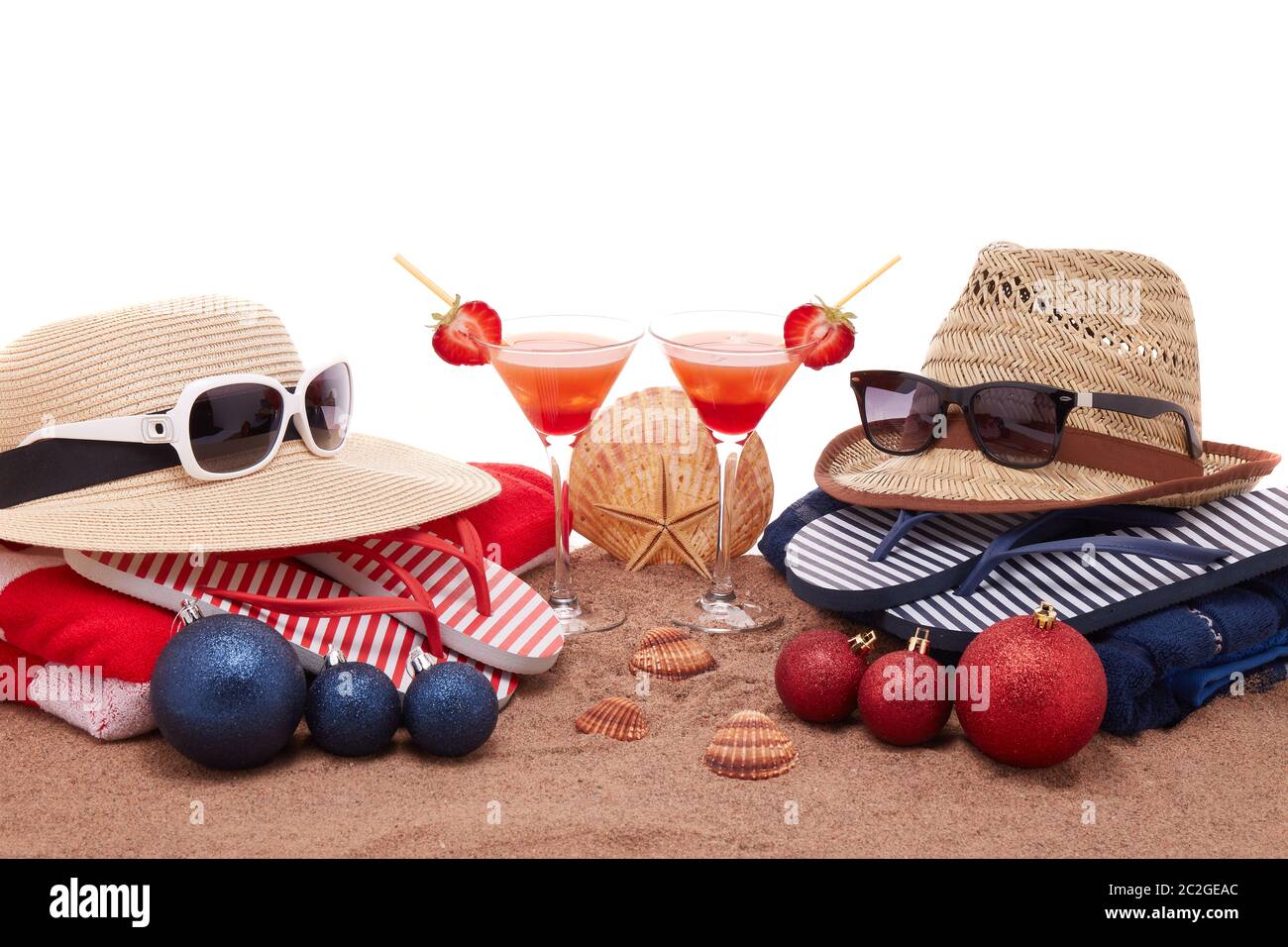 Beach accessories (flip flops, straw hats, seashells, sand, sunglasses), two glasses of cocktail, christmas ornaments on white background. Christmas. Stock Photo