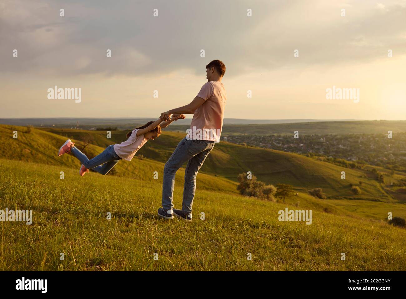 Young father playing game with his daughter in countryside at sunset, copy space. Dad spinning child in circles outdoors Stock Photo