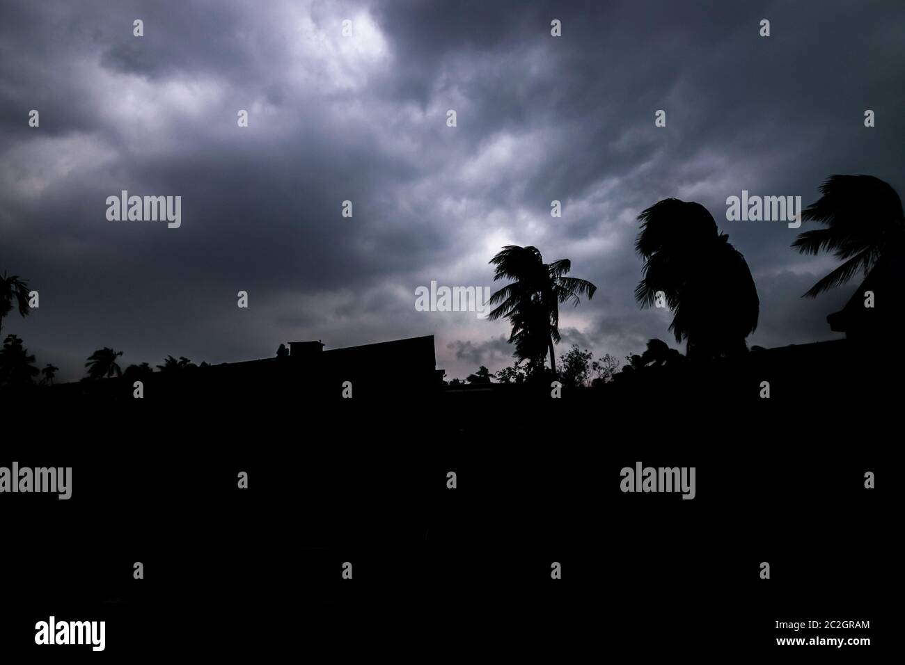 A silhouette of trees and houses with sky full of dark clouds above ...