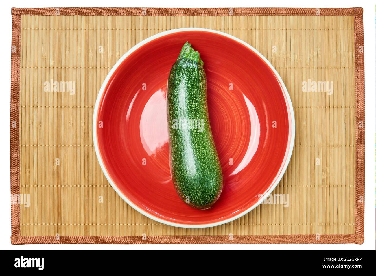 color contrasting still life - patterned green zucchini squash on a red plate on a cane serving mat Stock Photo