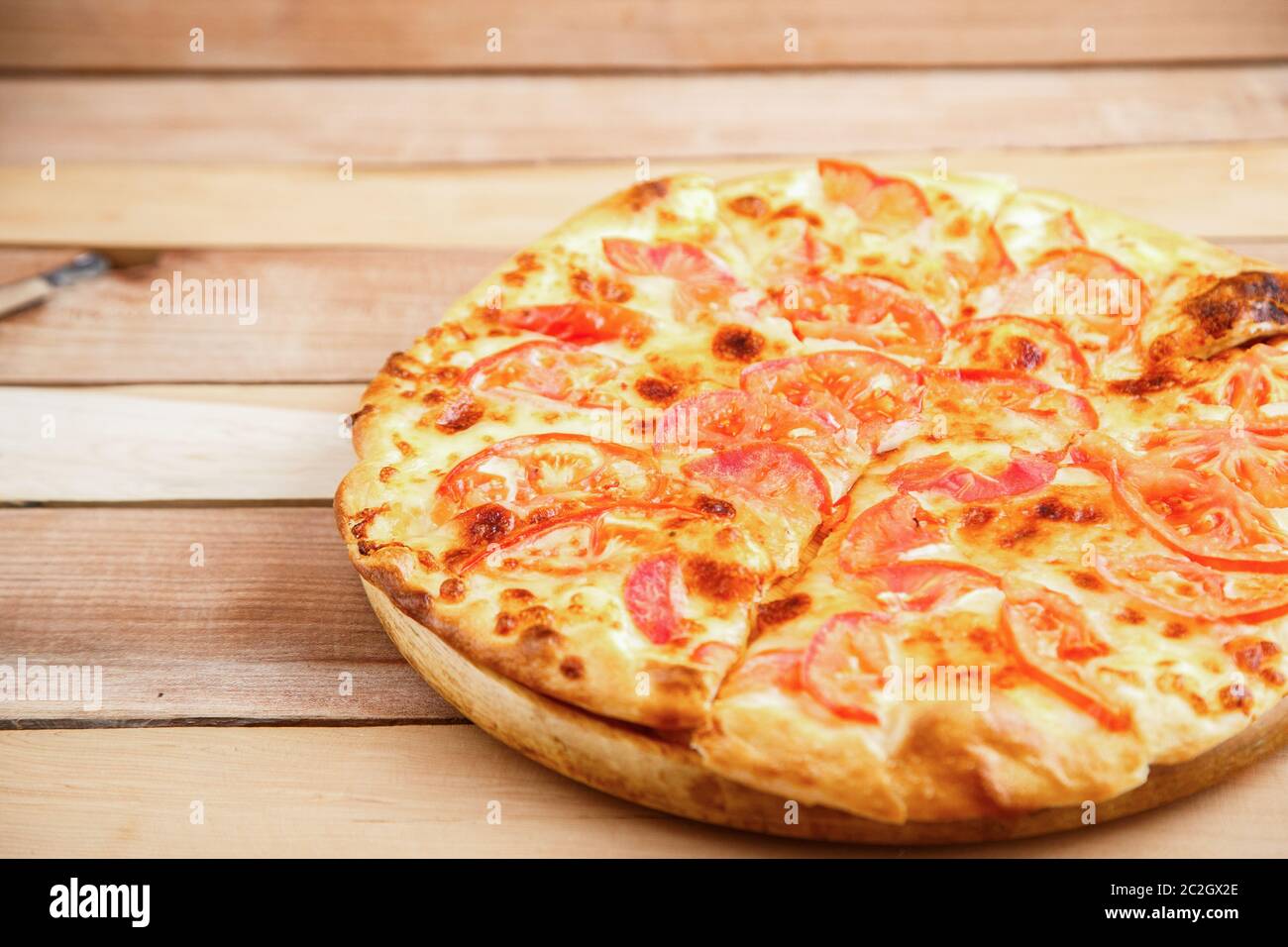 medium-sized pizza with tomatoes on a wooden tray Stock Photo