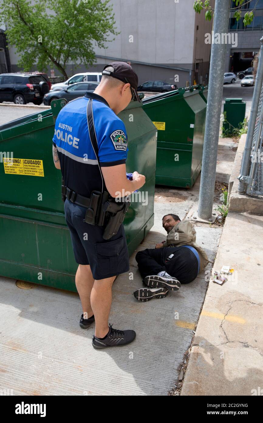 Homeless man sleeping by dumpster - A homeless man appears to be sleeping behind a trash receptacle in downtown Austin and is awakened by a police officer following a complaint by a landowner.  No arrests were made or tickets issued.   March 28, 2014 © Bob Daemmrich Stock Photo