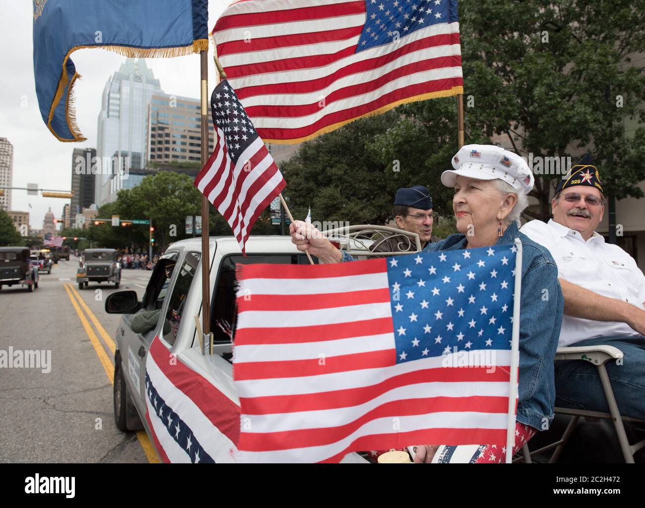 Austin Texas USA, November 11 2015: Woman waves American flag while sitting in the bed of a decorated pickup truck with other members of a local chapter of the American Legion during the annual Veterans Day parade up Congress Avenue.  ©Bob Daemmrich Stock Photo