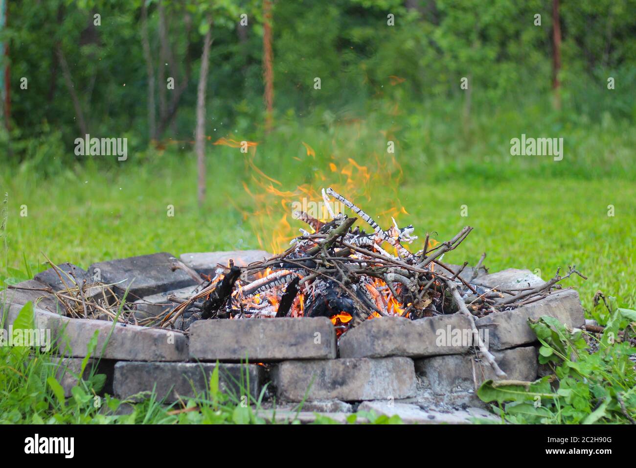 Tree branches burn in a bonfire in a round brick fireplace Stock Photo