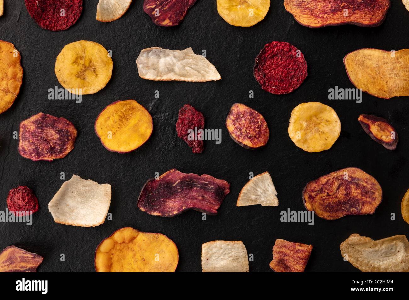 Dry fruit and vegetable chips, overhead shot. Healthy vegan snack, an organic food flat lay pattern on a black background Stock Photo