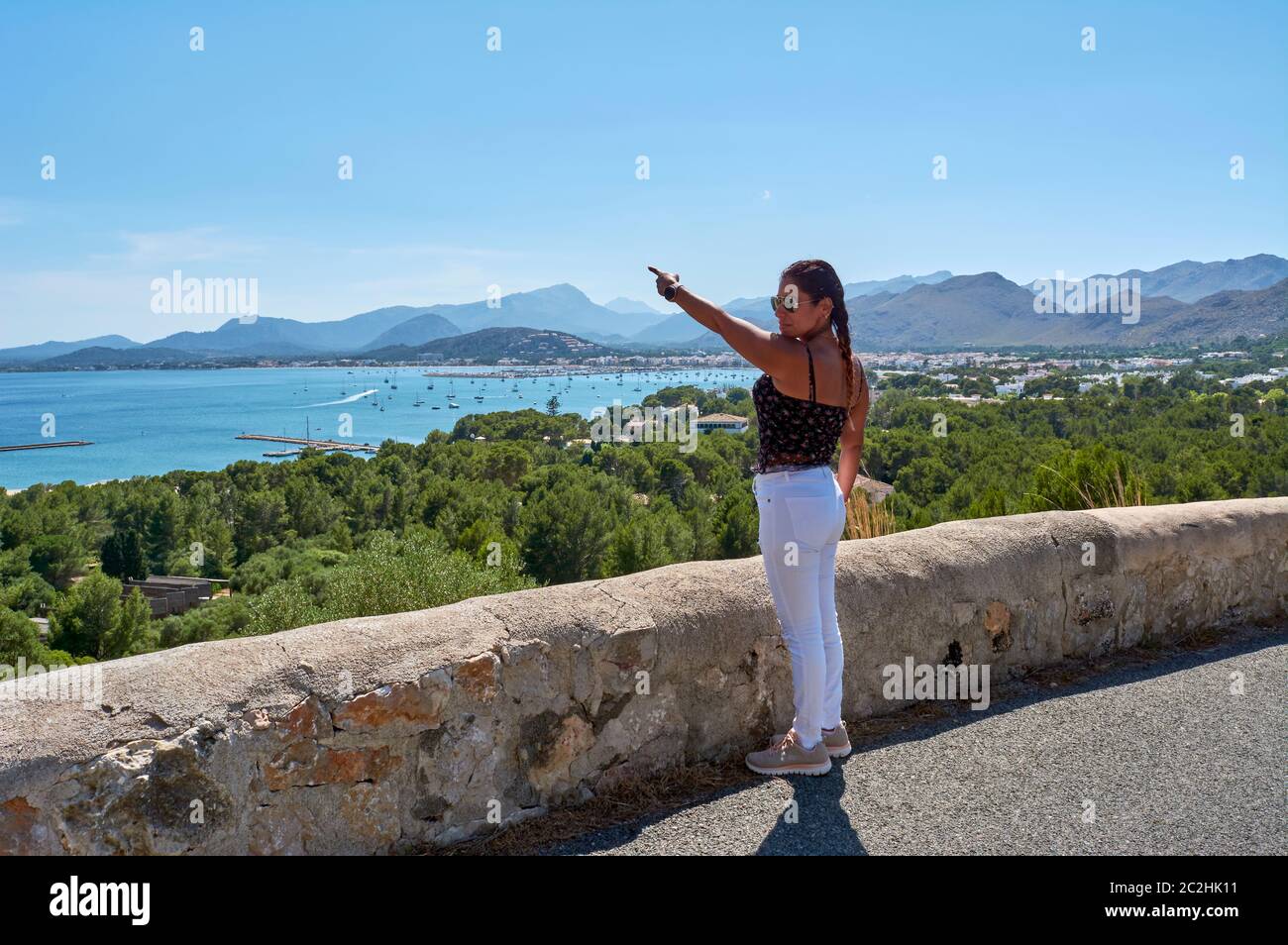 Latin woman, with long wavy brown hair on a spring day wearing sunglasses, on the road with a typical stone wall, indicating where she is, the Pollens Stock Photo