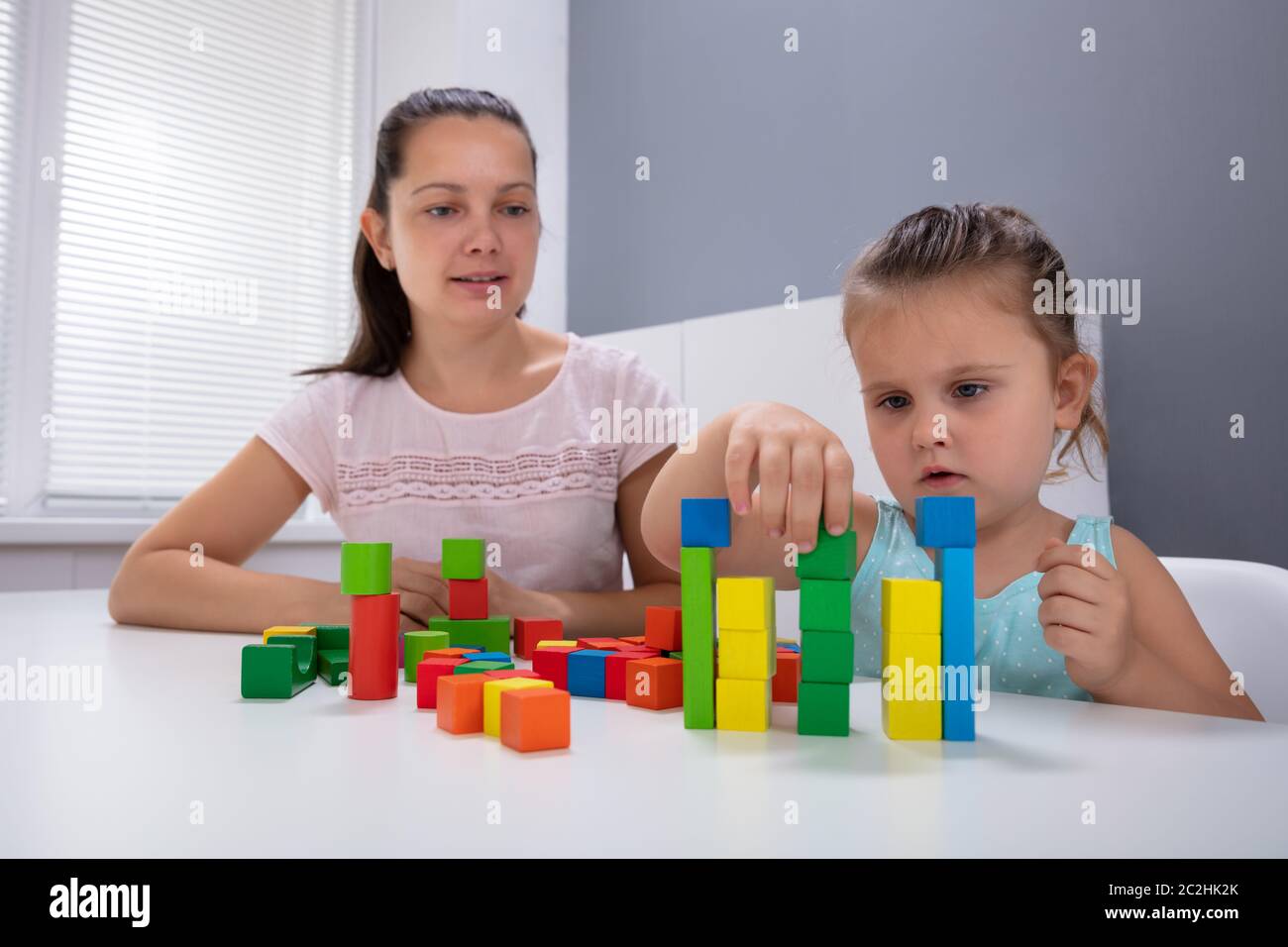 Smiling Daycare Worker Playing With Child Stacking Building Blocks On