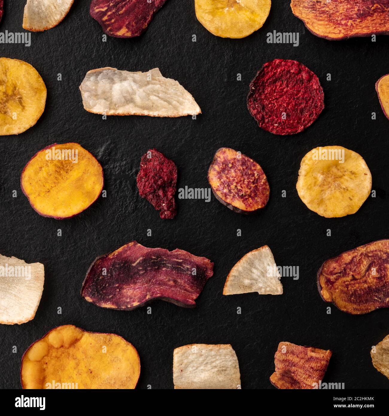 Dry fruit and vegetable chips, square top shot. Healthy vegan snack, an organic food flat lay pattern on a dark background Stock Photo