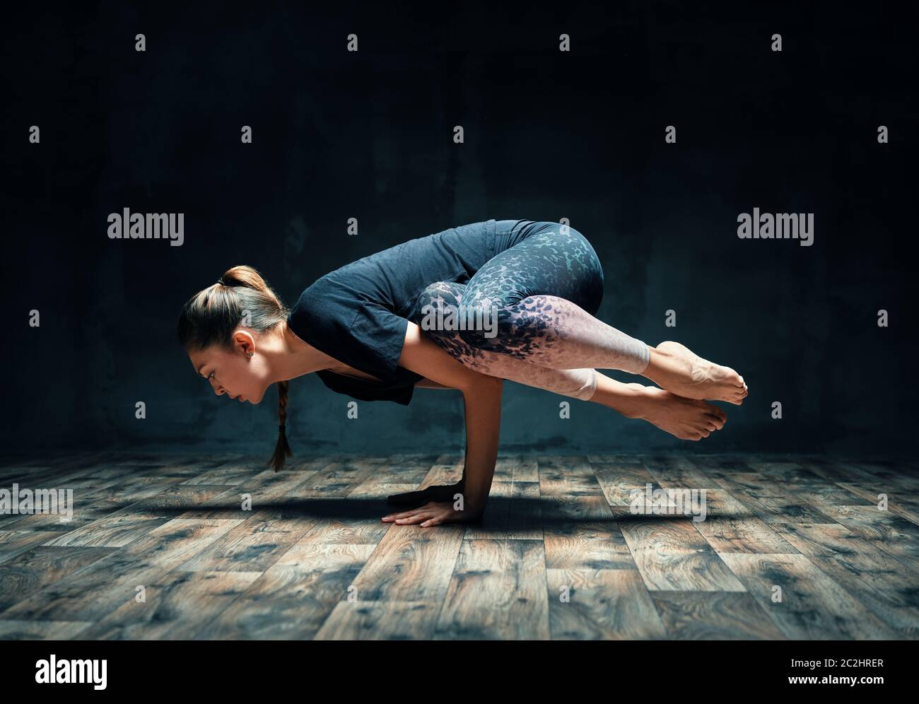 Young attractive woman practicing yoga doing side crane pose in dark room Stock Photo