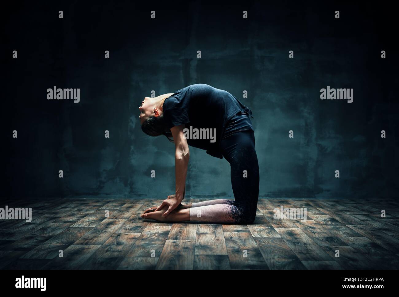 Young woman practicing yoga doing Camel pose in dark room Stock Photo