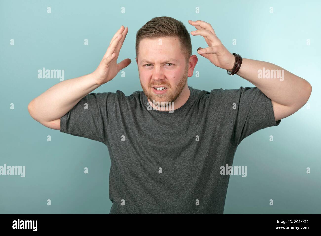 Frustrated angry man snarling and gesturing with his hands either side of his head over a grey background Stock Photo