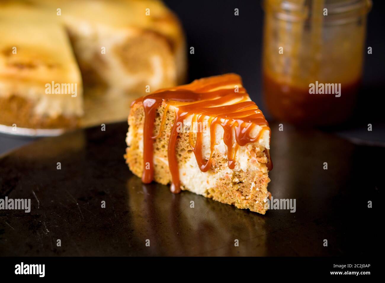 Slice of marble cake that is a mix of carrot cake and cheesecake swirled together and topped with caramel sauce. A delicious sweet creamy dessert. Stock Photo