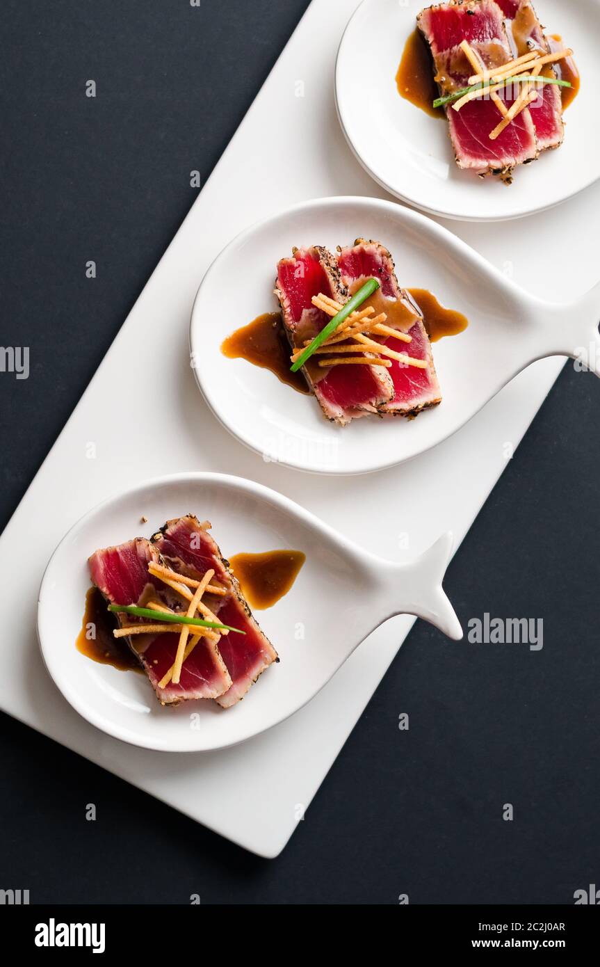 Tuna Tataki is a Japanese dish which consist of briefly seared tuna steak in thin slices. Served as appetizer with brandy sauce and garnish on a dark Stock Photo