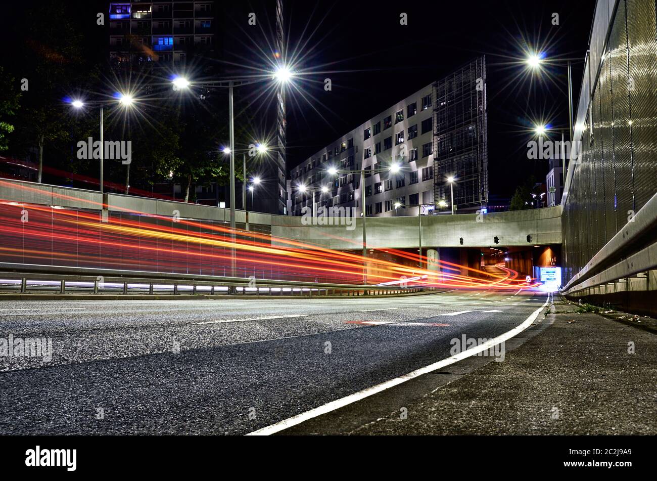 Tunnel opening in city with car trails surrounded by asphalt and concrete with modern buildings Stock Photo