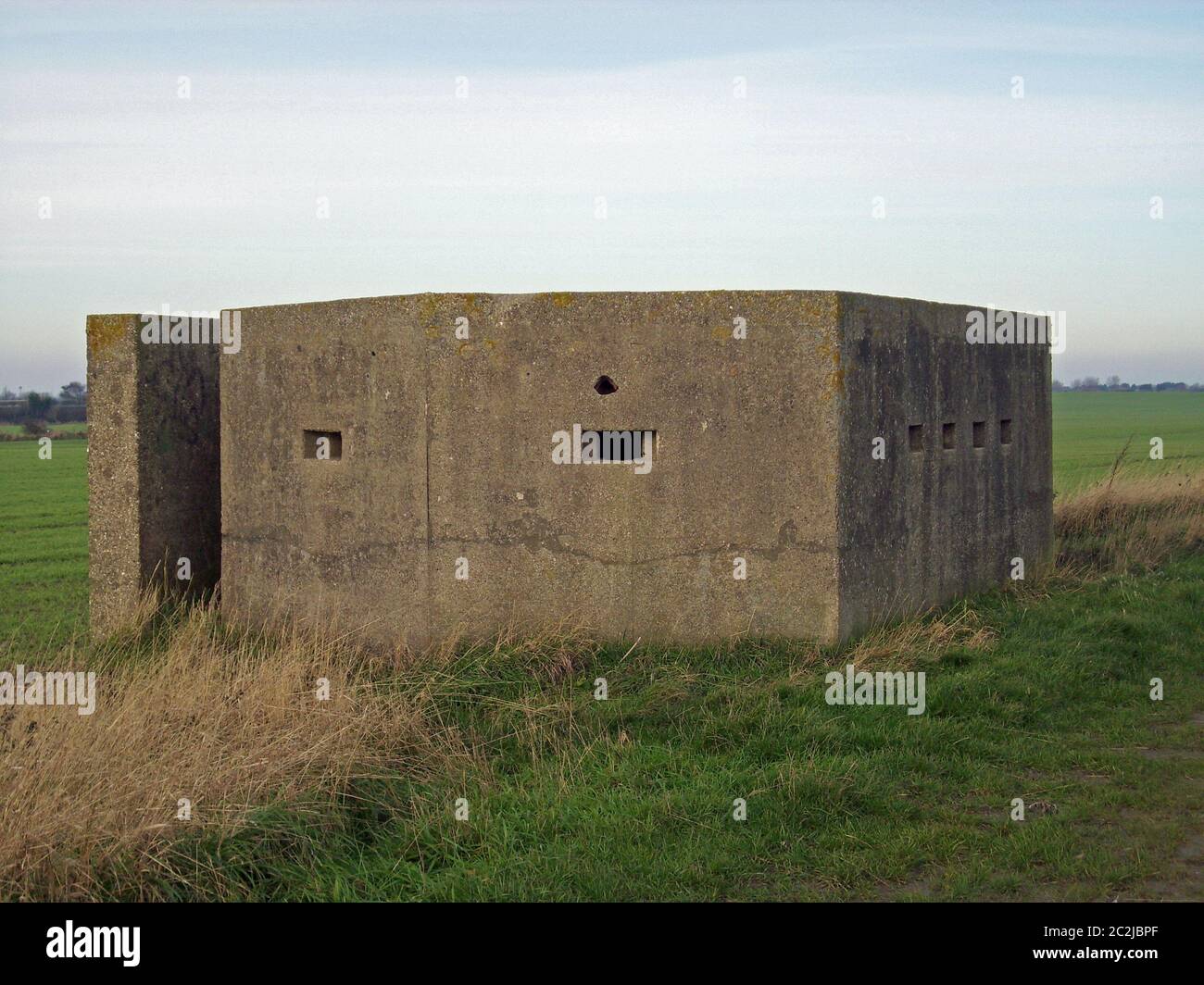 World War Two concrete pillbox on the east coast of Yorkshire, England. Rear entrance and loopholes visible. Surrounded by grass. Blue sky with white Stock Photo