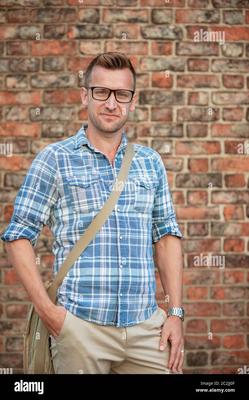 A man standing in front of a brick wall and looking into the camera ...
