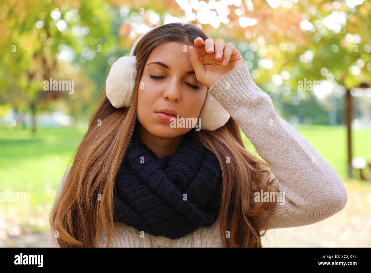 Girl with earmuffs suffering migraine headache fever outdoors Stock