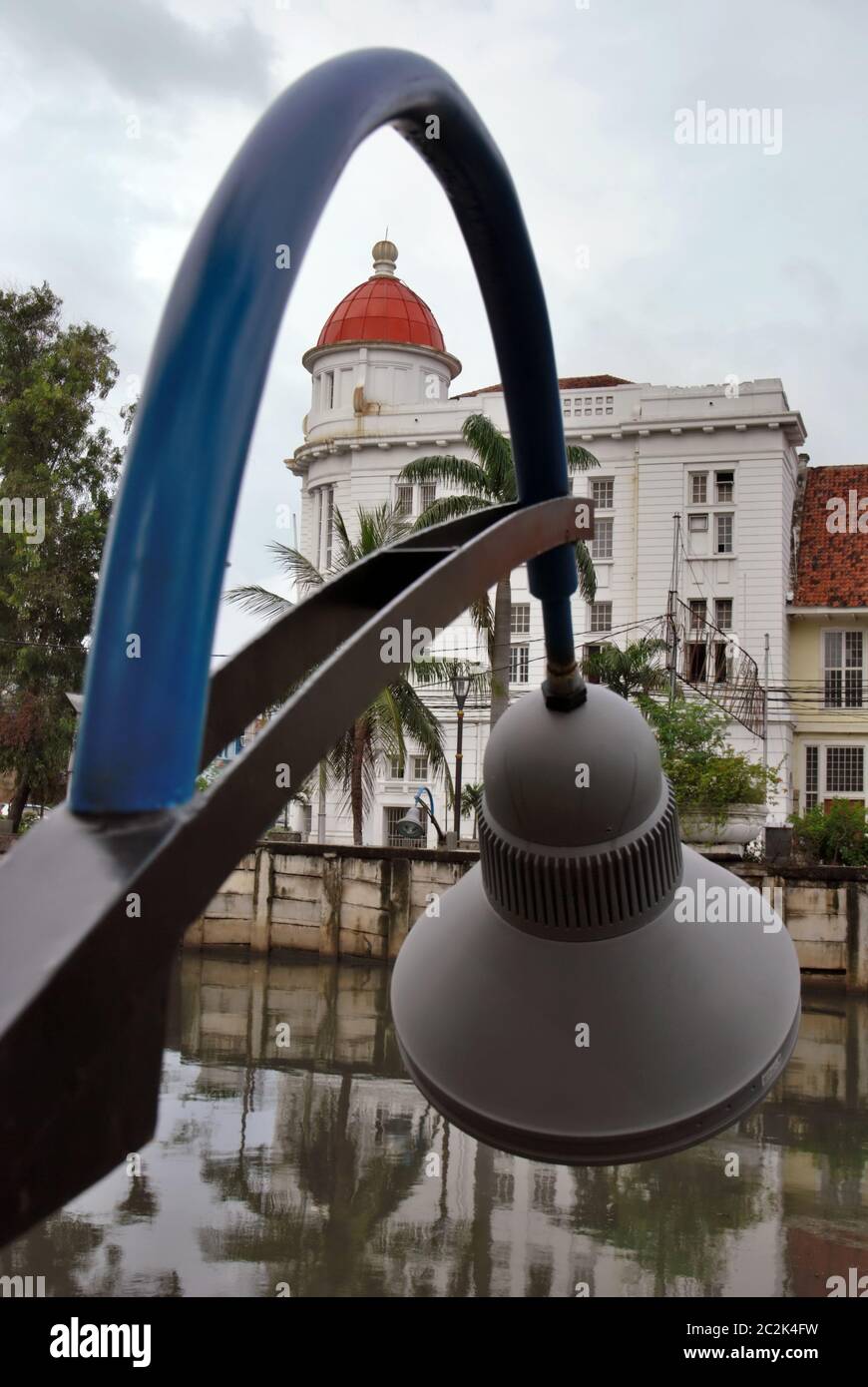 A building with old architectural style seen through streetlight installation on the side of canal in Jakarta Old Town area. Jakarta, Indonesia. Stock Photo