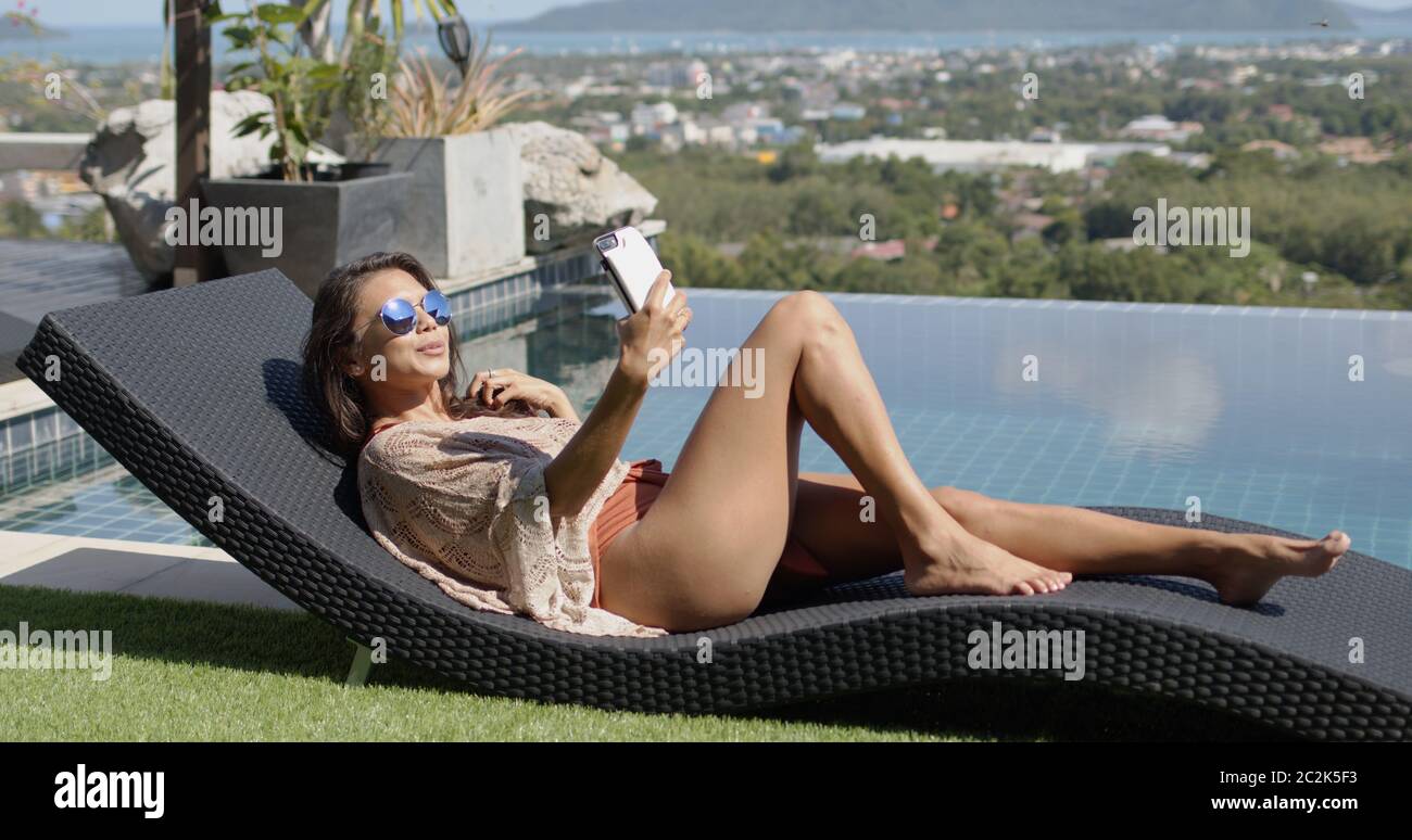 Lounging female taking selfie at poolside on top of hotel Stock Photo