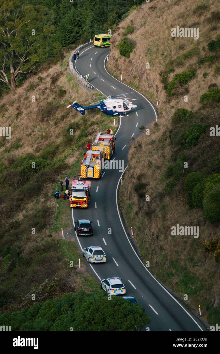A rescue helicopter is parked on the road while emergency services work to free the driver of a vehicle down a hill in Christchurch, New Zealand Stock Photo