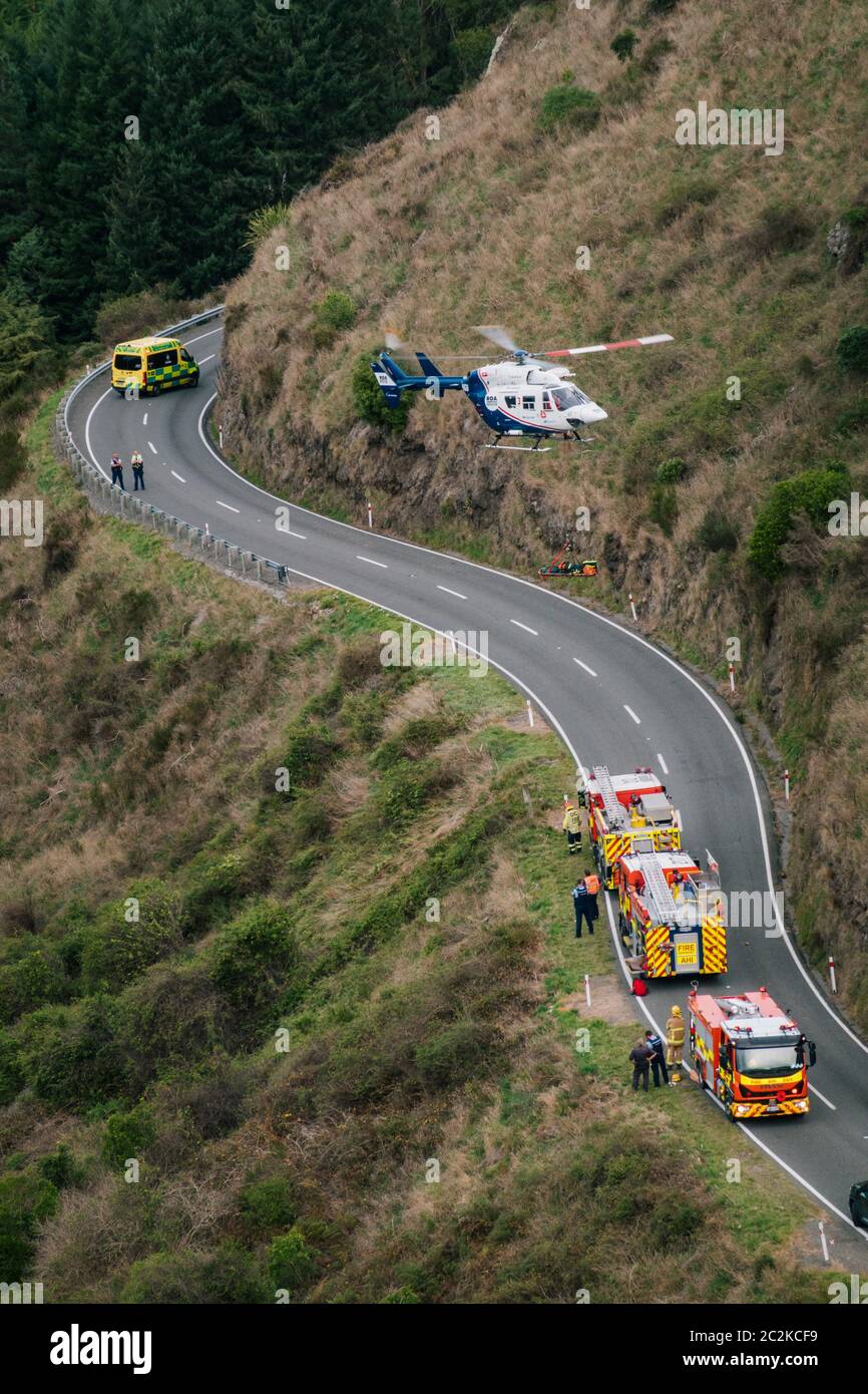 A rescue helicopter lowers a stretcher piled with extrication equipment onto the road next to waiting emergency services Stock Photo