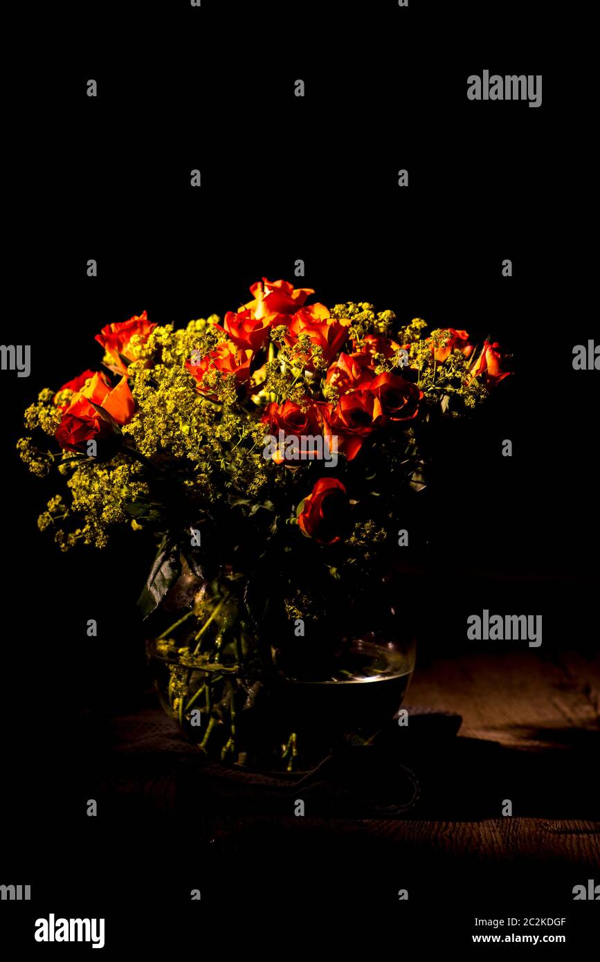 oranger Rosenstrauß in Glasvase vor dunklem Hintergrund Stock Photo