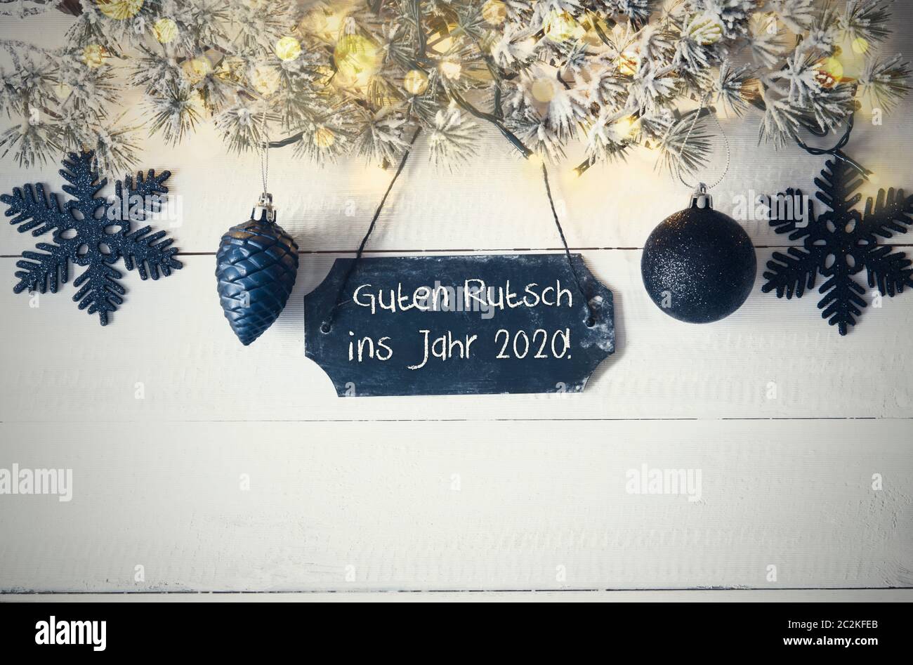 Black Chirstmas Plate With German Text Guten Rutsch Ins Jahr 2020 Means Happy New Year 2020. Fir Branch With Fairy Lights On Wooden Background. Black Stock Photo