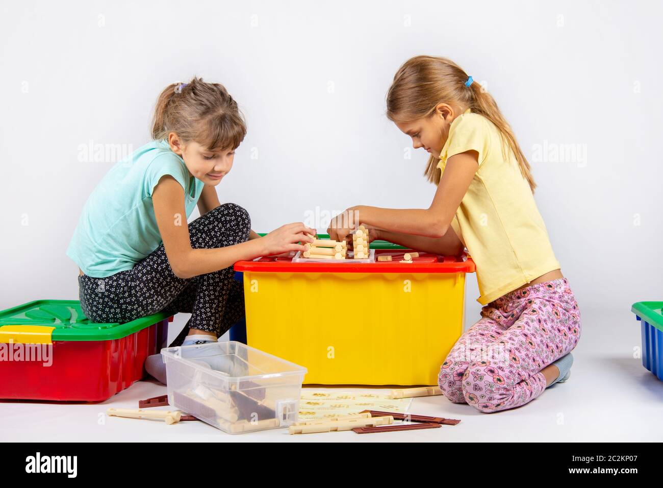 Two girls are assembling a house on a box with toys, looking in the ...