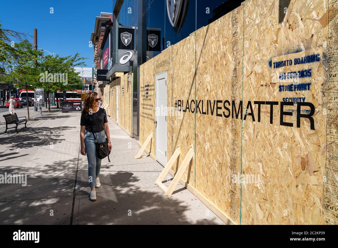 Young woman walking on the streets of Toronto looking at boarded up storefront with Black Lives Matter message supporting movement against injustice. Stock Photo