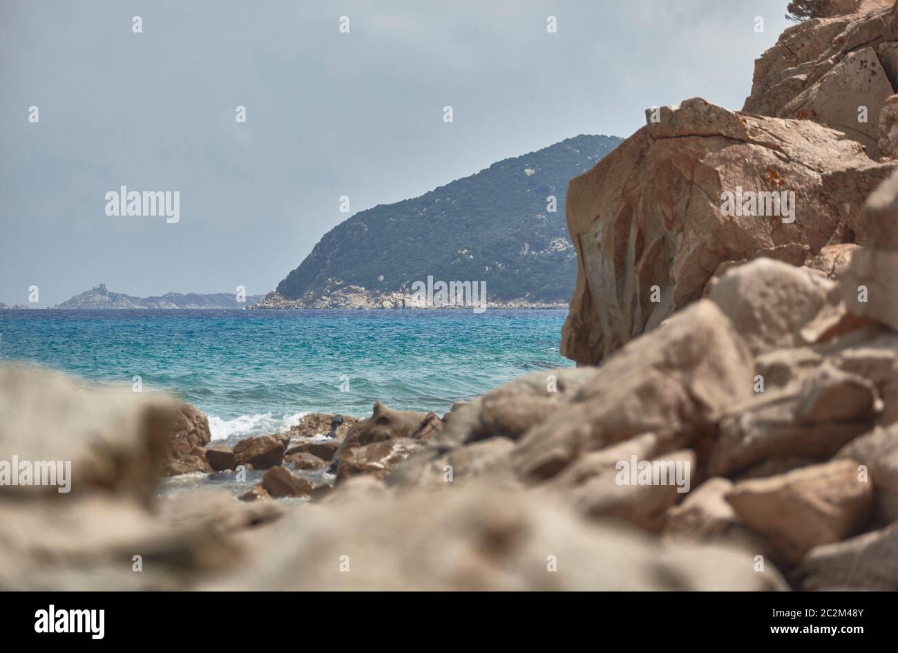 Mountain overlooking the sea filtered by some blurred rocks nearby. Stock Photo