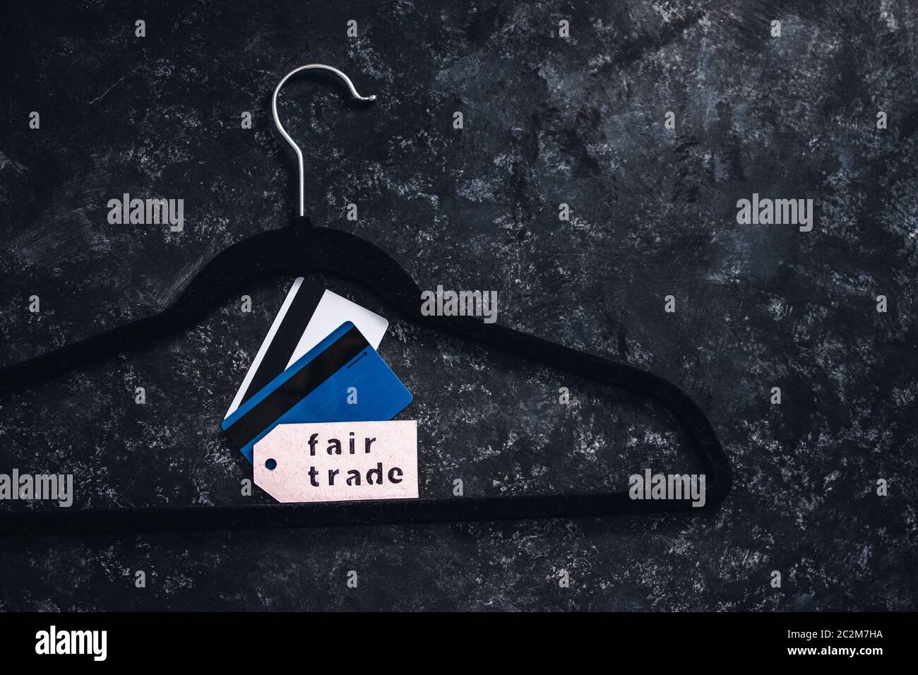ethical fashion concept, velvet clothes hanger with Fair Trade label and credit cards on it on black background Stock Photo