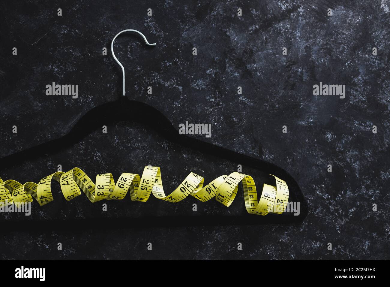 Fashion Industry And Risks Of Eating Disorders Concept Velvet Hanger With Yellow Measuring Tape 