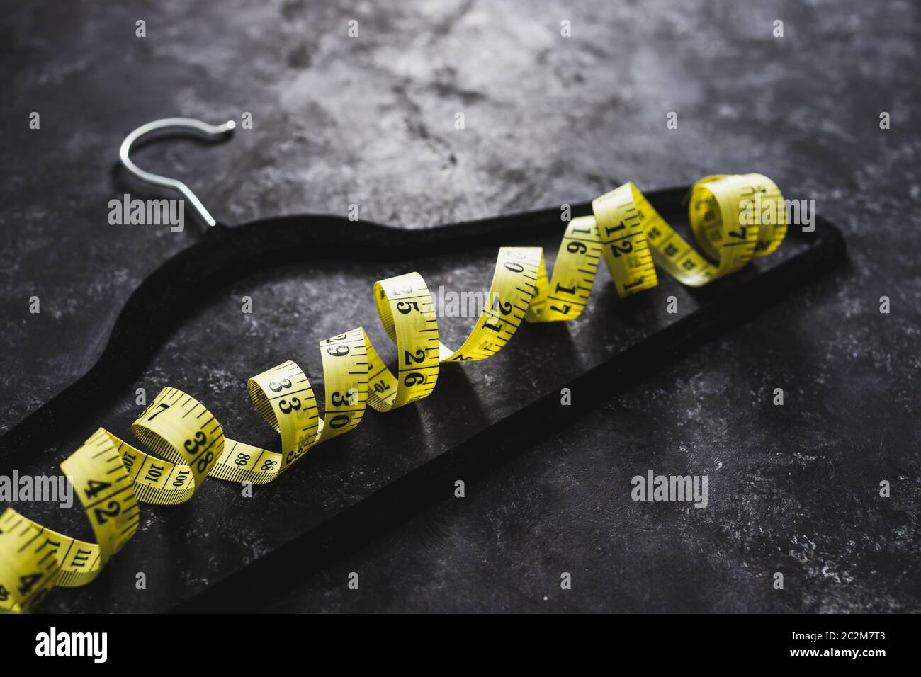 Fashion Industry And Risks Of Eating Disorders Concept Velvet Hanger With Yellow Measuring Tape 