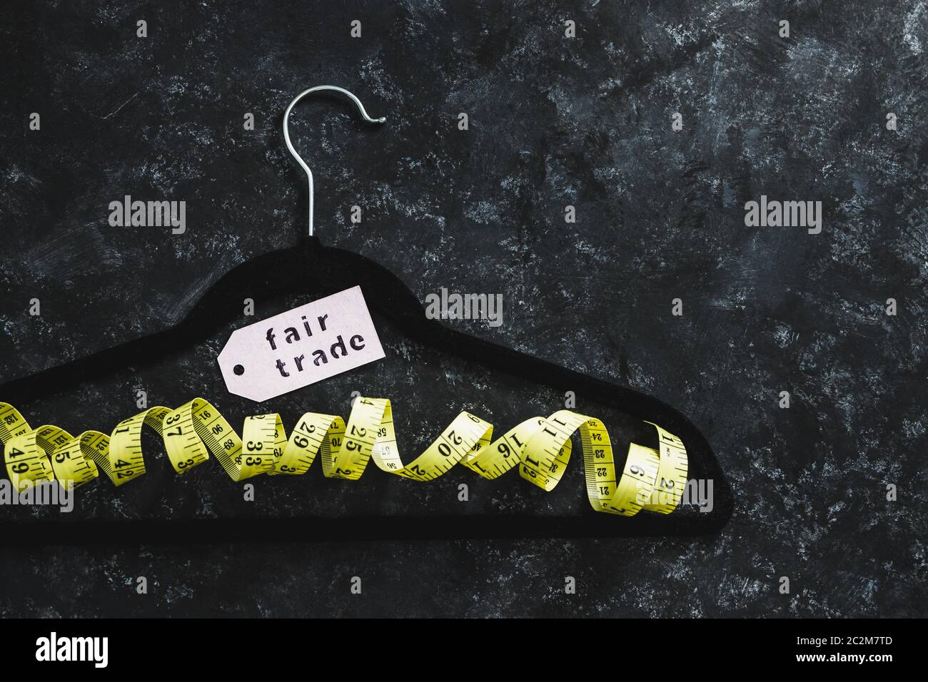 fashion industry and ethical products concept, velvet hanger with yellow measuring tape and Fair Trade label on it on black background Stock Photo