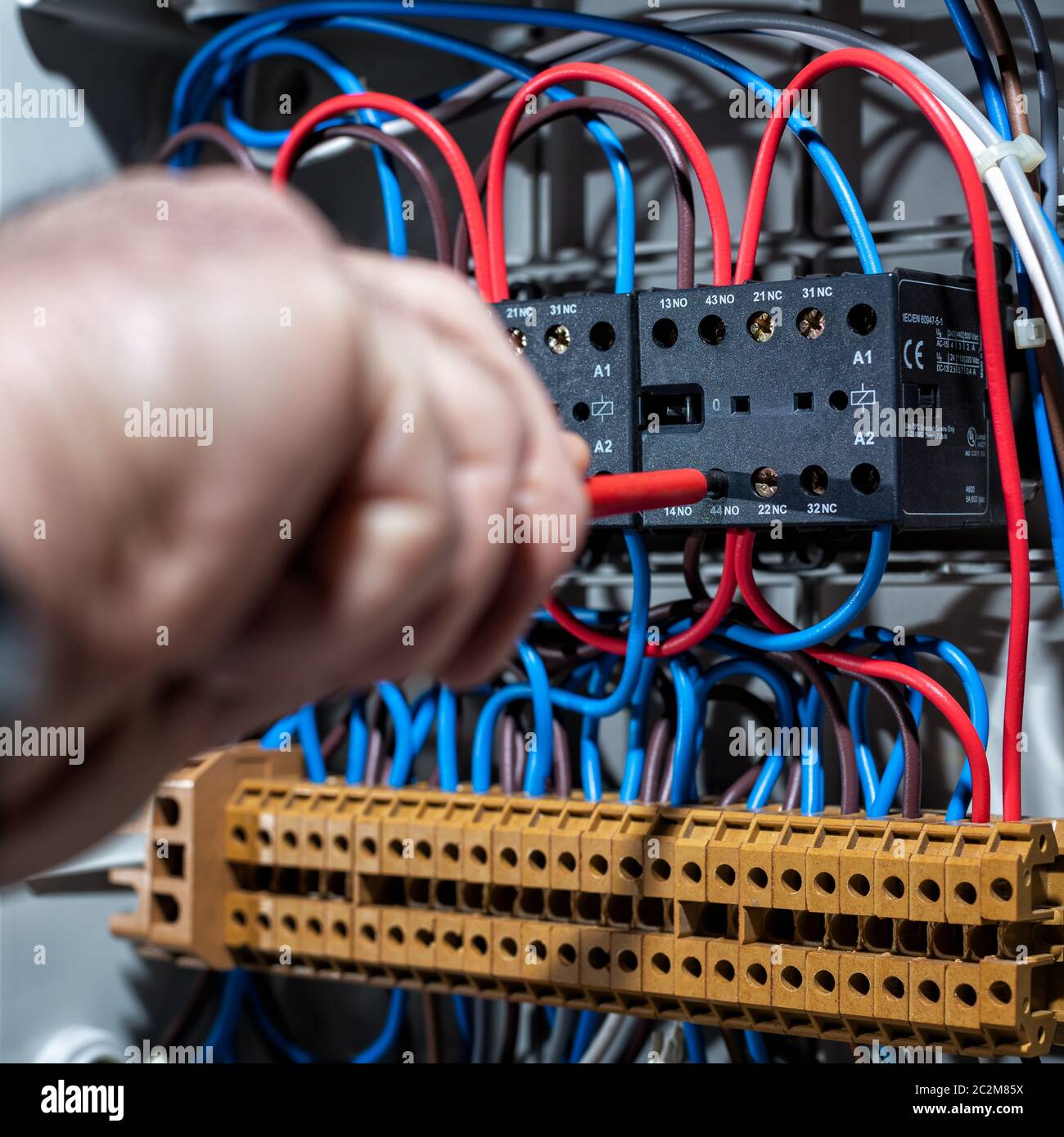 Electrician with screwdriver fixes the cable in a residential electrical distribution panel