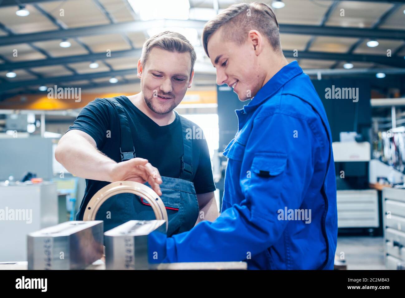 Skillful master discussing a workpiece with his apprentice or trainee Stock Photo