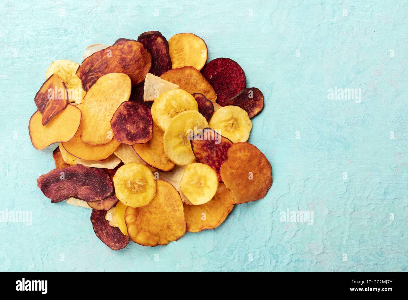 Dried fruit and vegetable chips, healthy vegan snack, a mixed heap on a teal background, top shot with a place for text Stock Photo