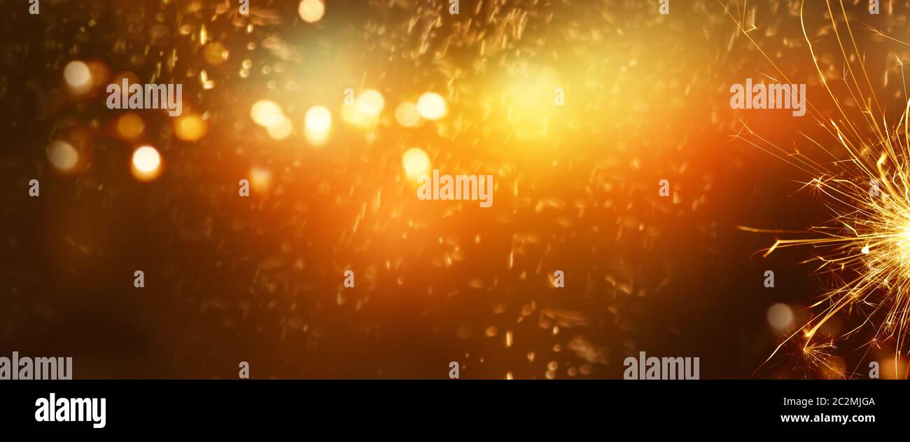 Fiery new years eve background with golden bokeh and sparkler for new year greetings Stock Photo