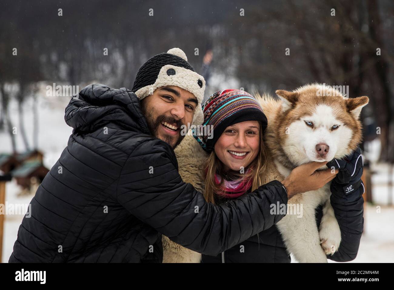 couple carrying a siberian dog in winter surrounded by snow. Stock Photo