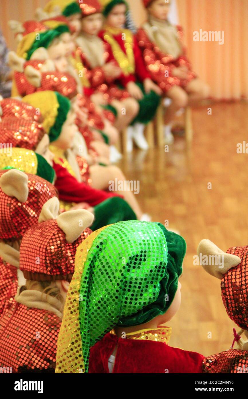 Children in fancy dresses on matinee at kindergarten. Children in smart suits sit on chairs during p Stock Photo