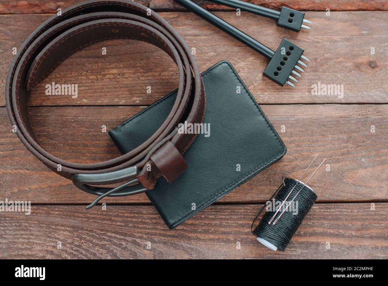 Black mens wallet and leather belt on wooden desk with leather tools, top view Stock Photo