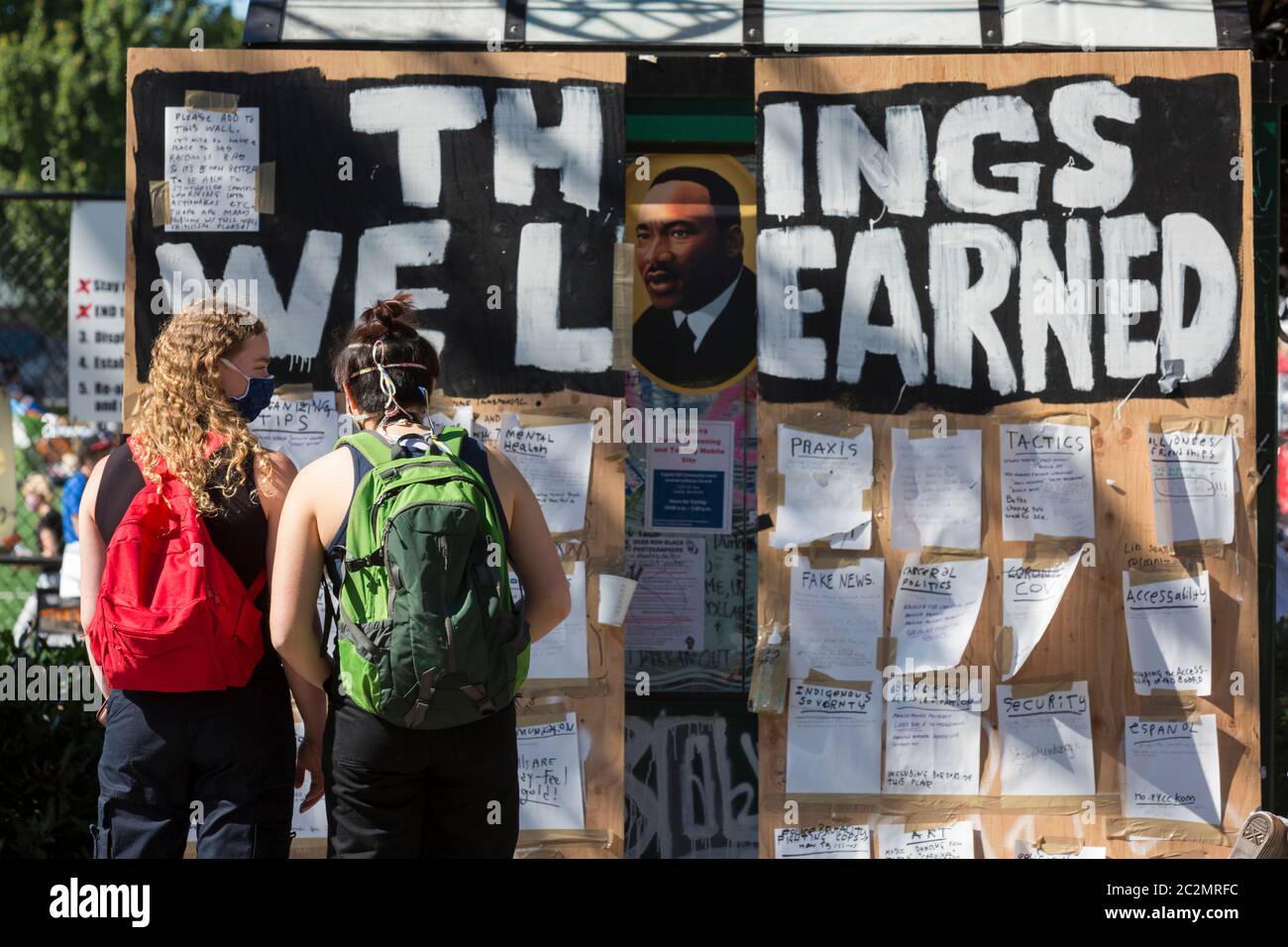 Two young women pause at a message board that reads 'things we learned' in the Capitol Hill Occupied Protest zone in Seattle on Wednesday, June 16, 2020. The zone, an occupation protest and self-declared autonomous zone, was established on June 8, 2020 when the Seattle Police Department closed the East Precinct after days of protests in the wake of the death of George Floyd while in Minneapolis police custody. Stock Photo