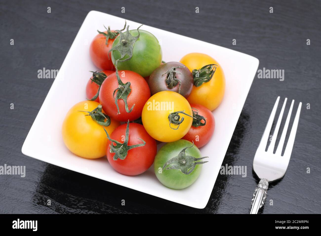colorful tomato on a plate on black background Stock Photo