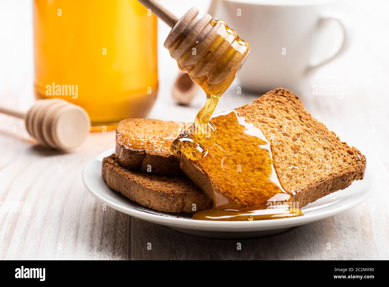 Honey dripping from wooden dipper on some wholemeal rusks. Stock Photo