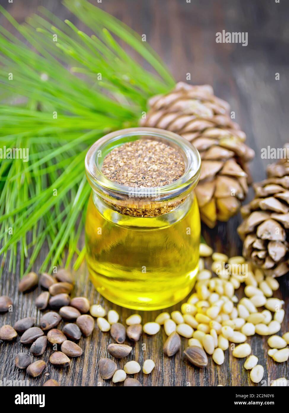 Cedar oil in a jar, two cedar cones, nuts and green twigs on a wooden board background Stock Photo