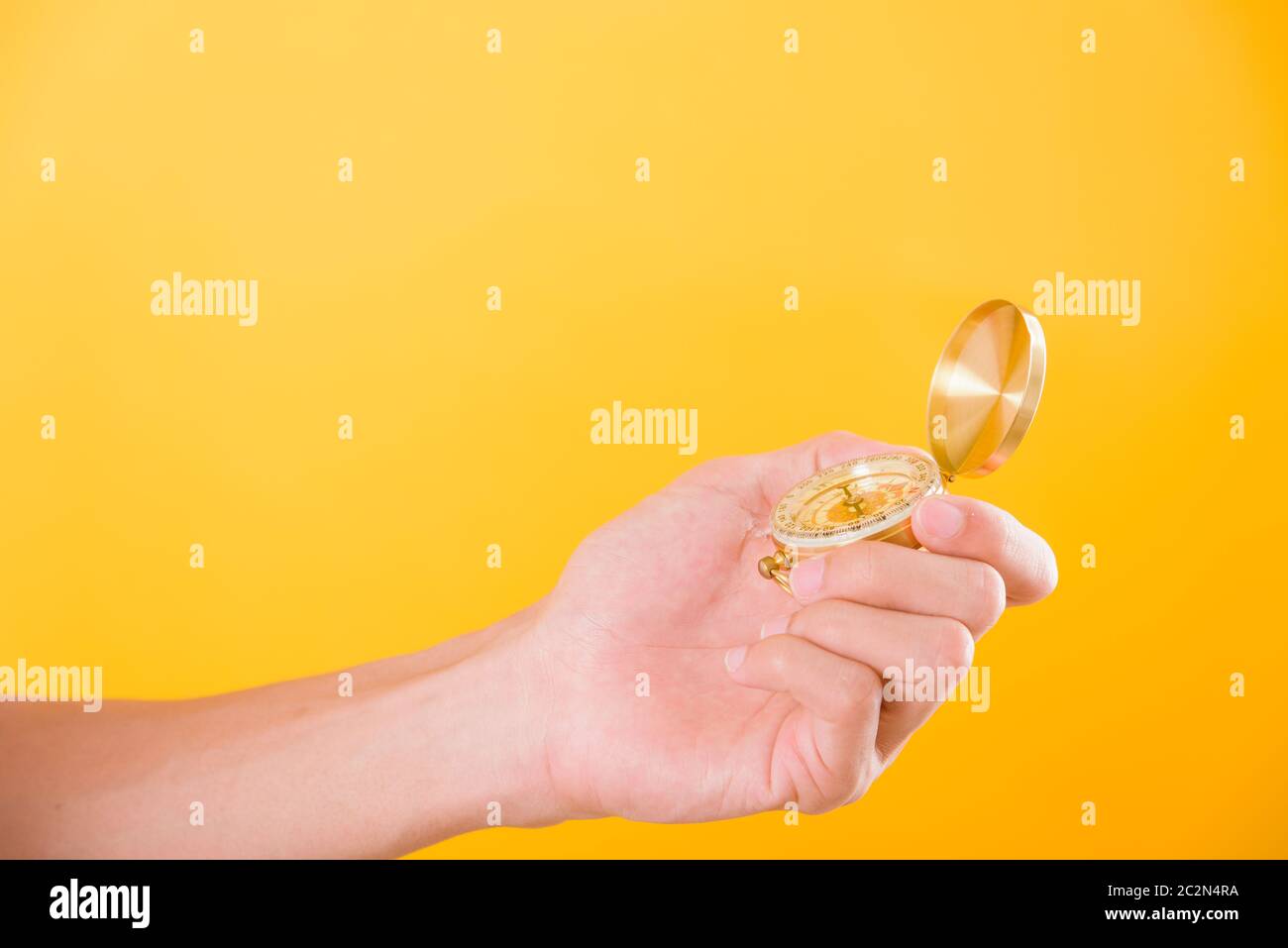 Hand holding antique brass compass isolated on yellow background with copy space for text Stock Photo
