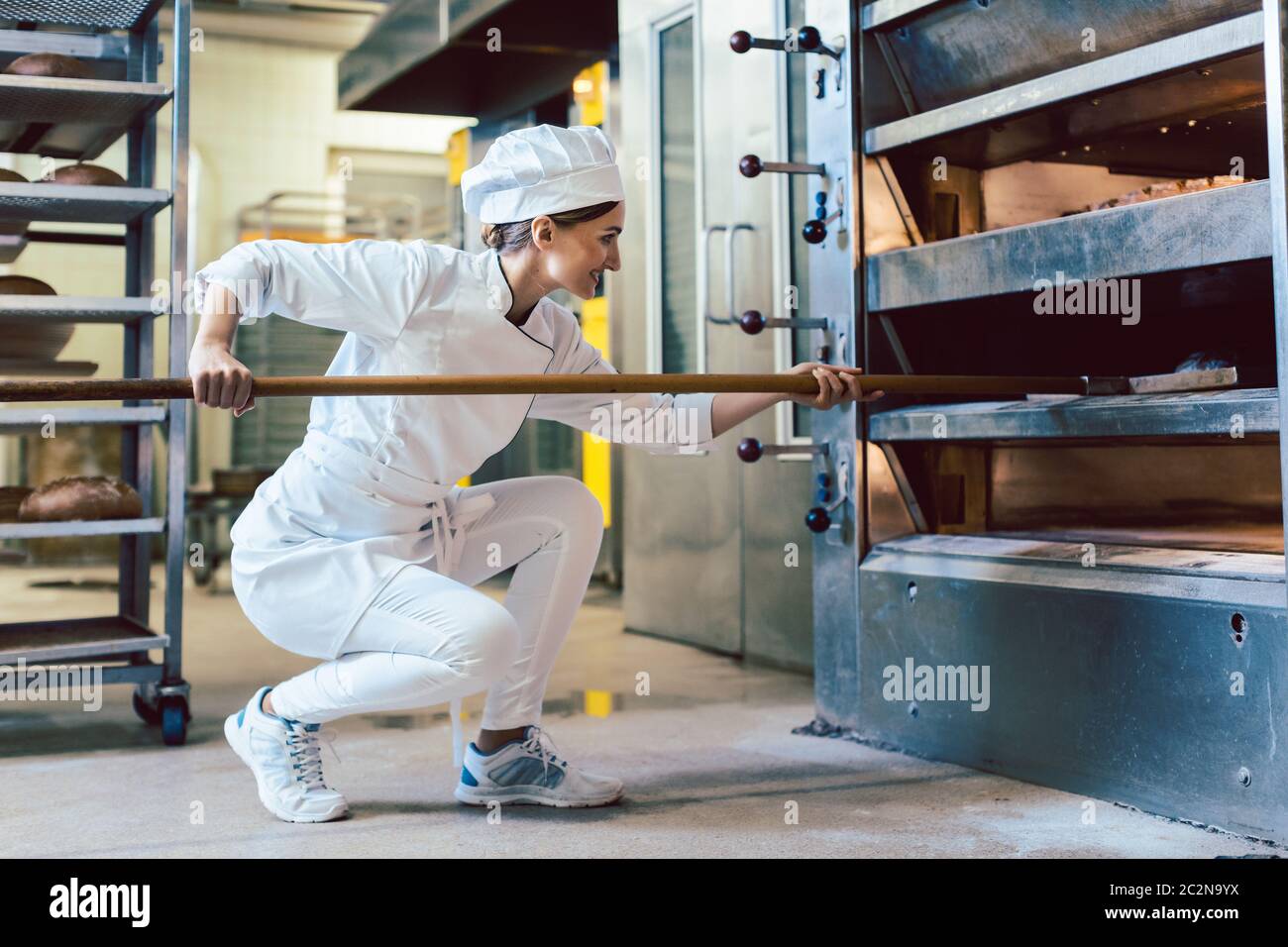 Baker putting bread in the bakery oven cowering on the floor of the bakery Stock Photo